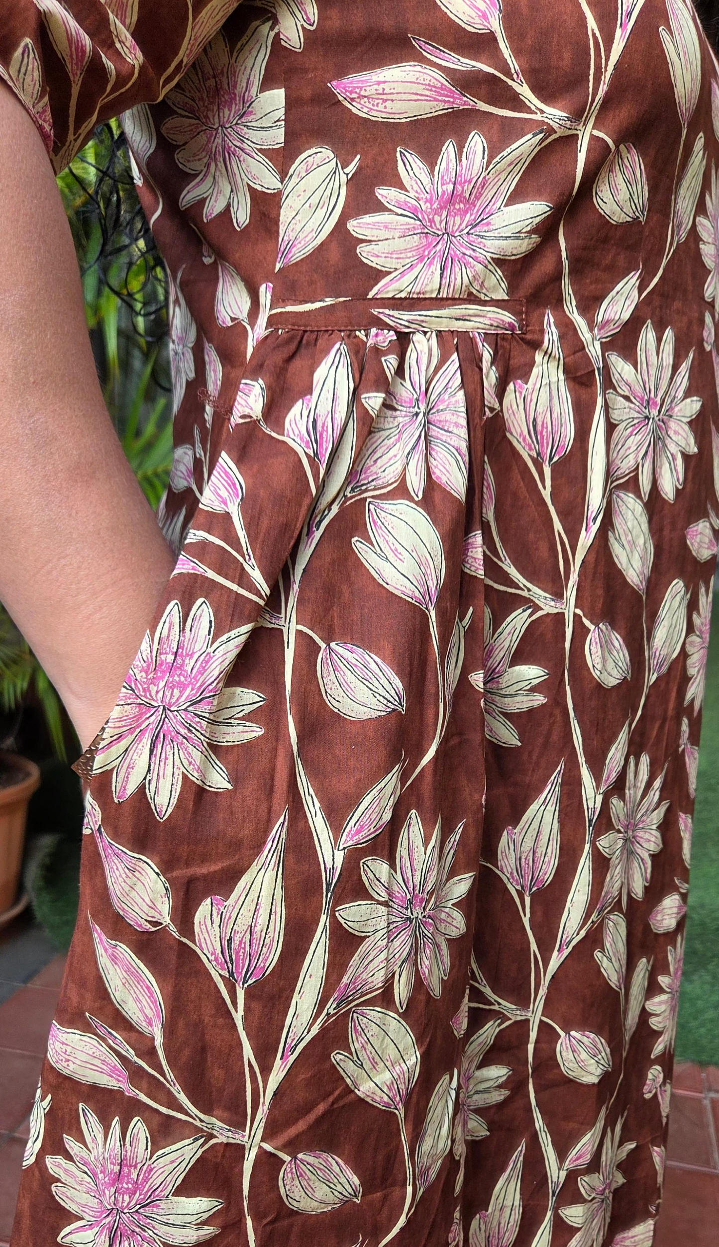Brown dress with floral pattern with pockets worn by a person, with a blurred background.