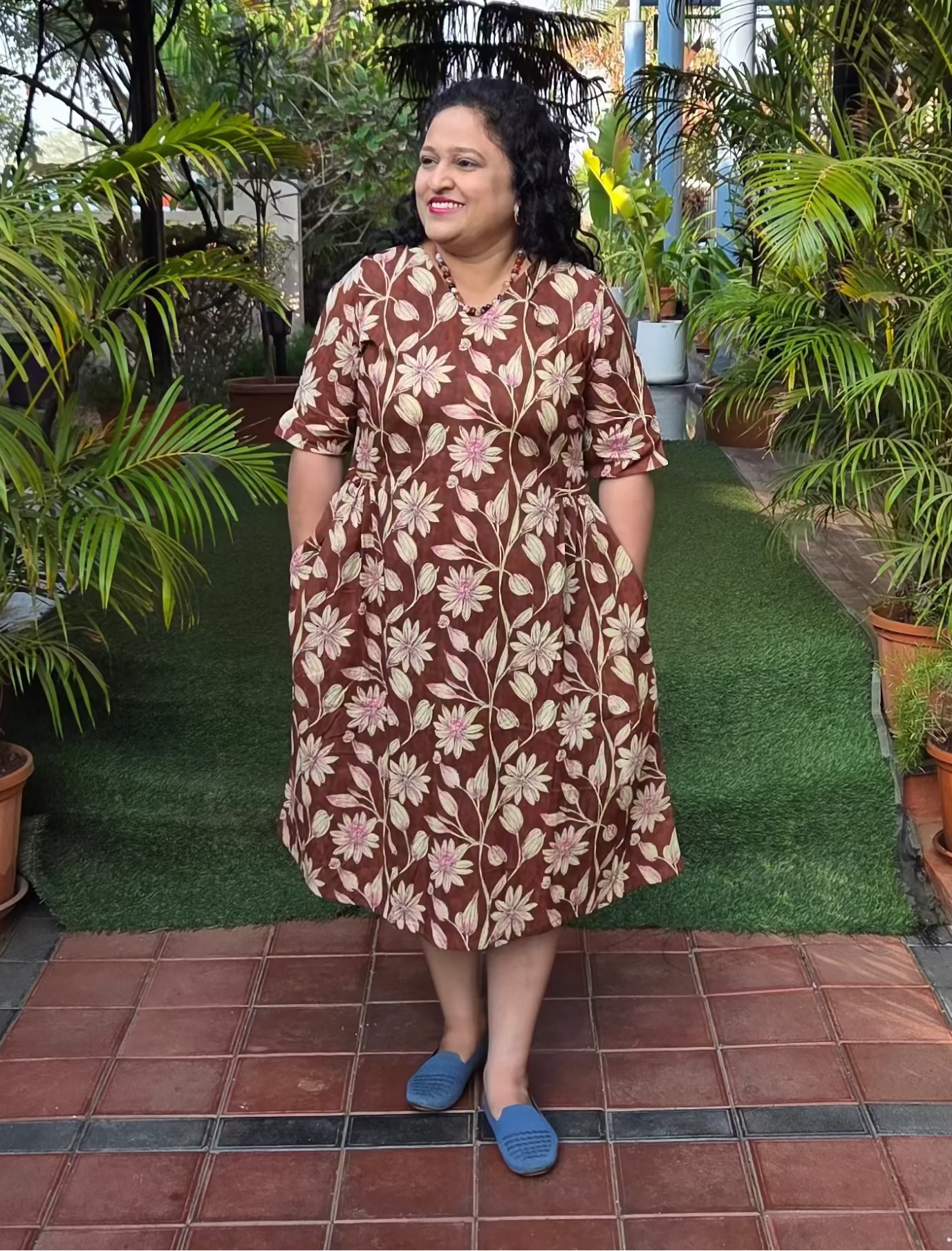 Woman in a patterned dress standing on a tiled path with greenery around
