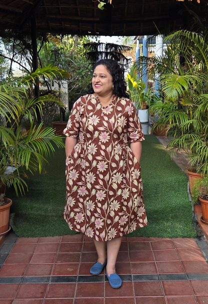 Woman in a patterned dress with 2 Pockets standing on a tiled path with greenery around