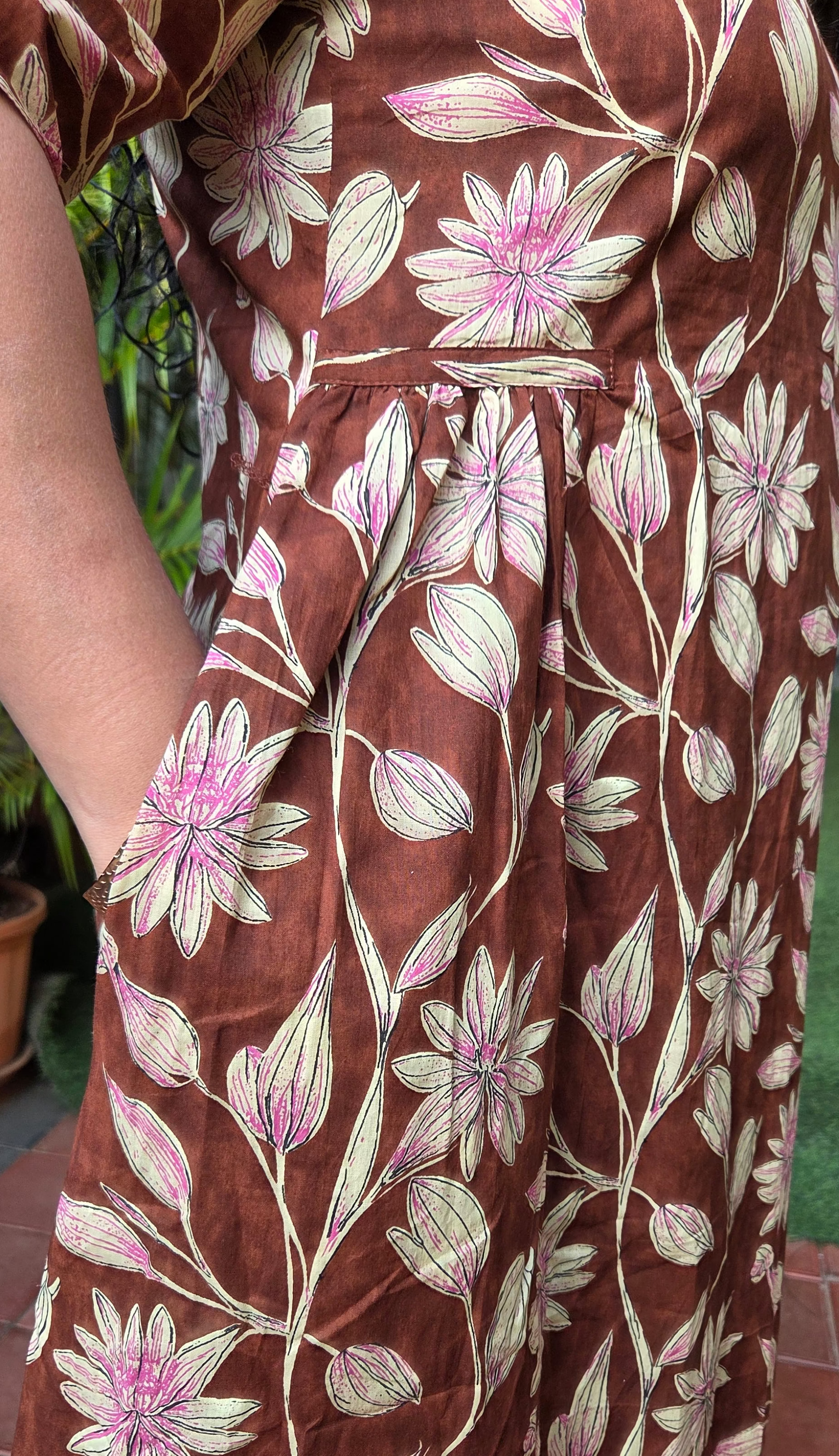 Brown dress with floral pattern with pockets worn by a person, with a blurred background.