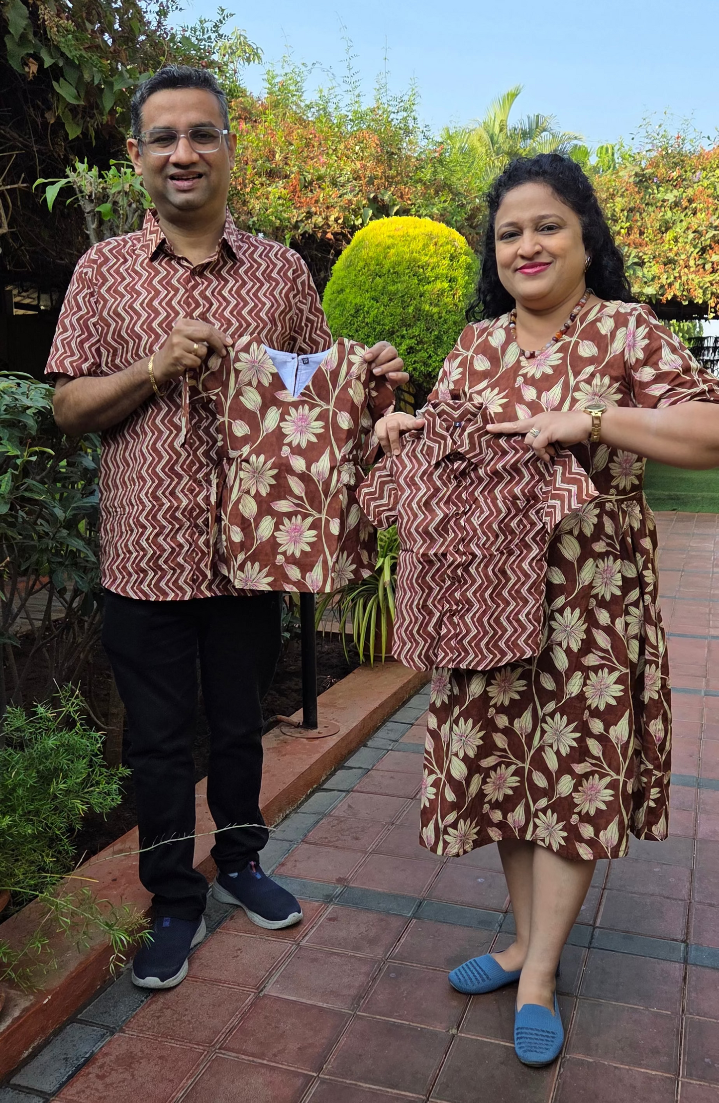 Couple holding patterned shirt and Frock in twinning pattern outdoors on a sunny day. 